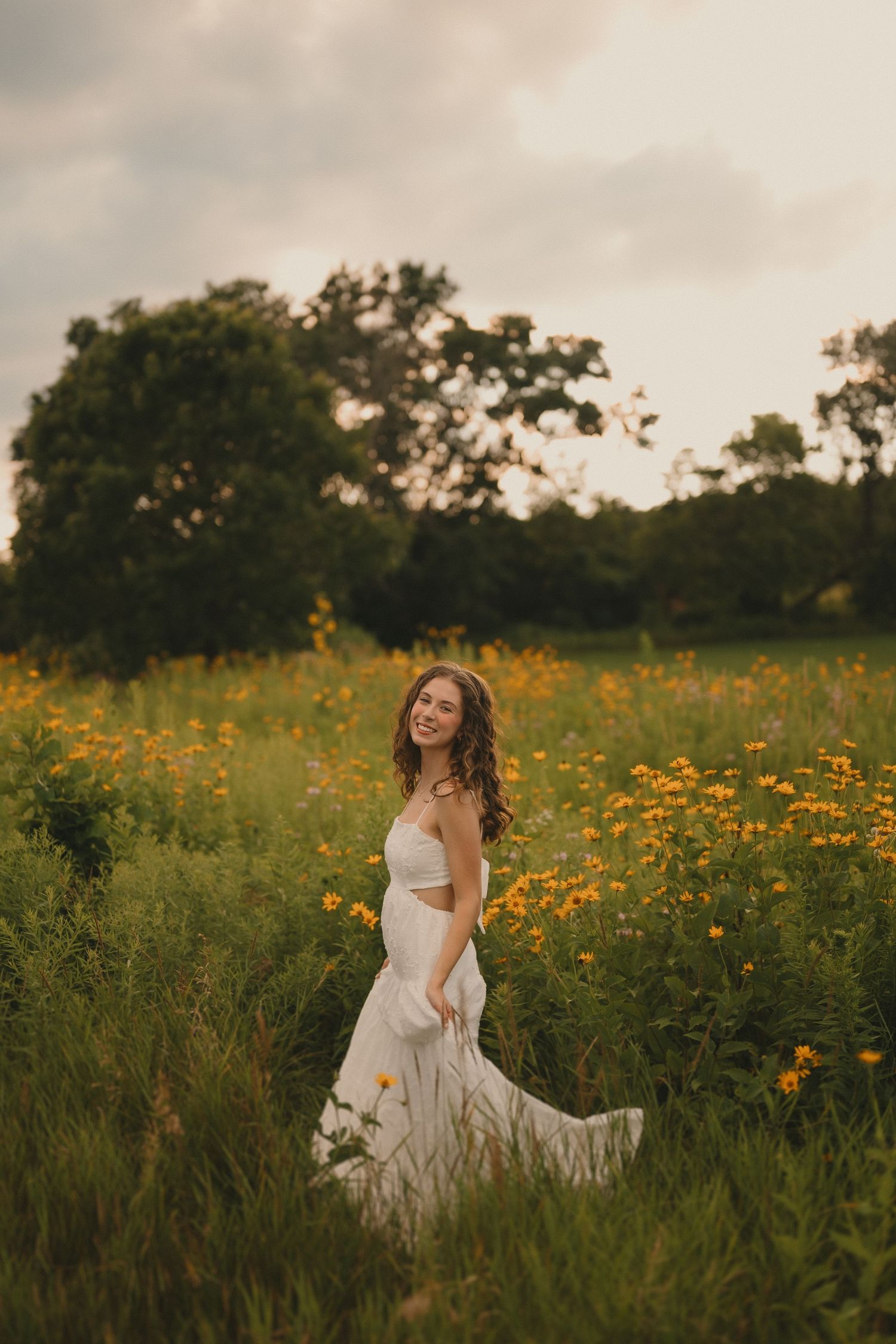 A flowing white dress twirls gracefully among yellow wildflowers at sunset.