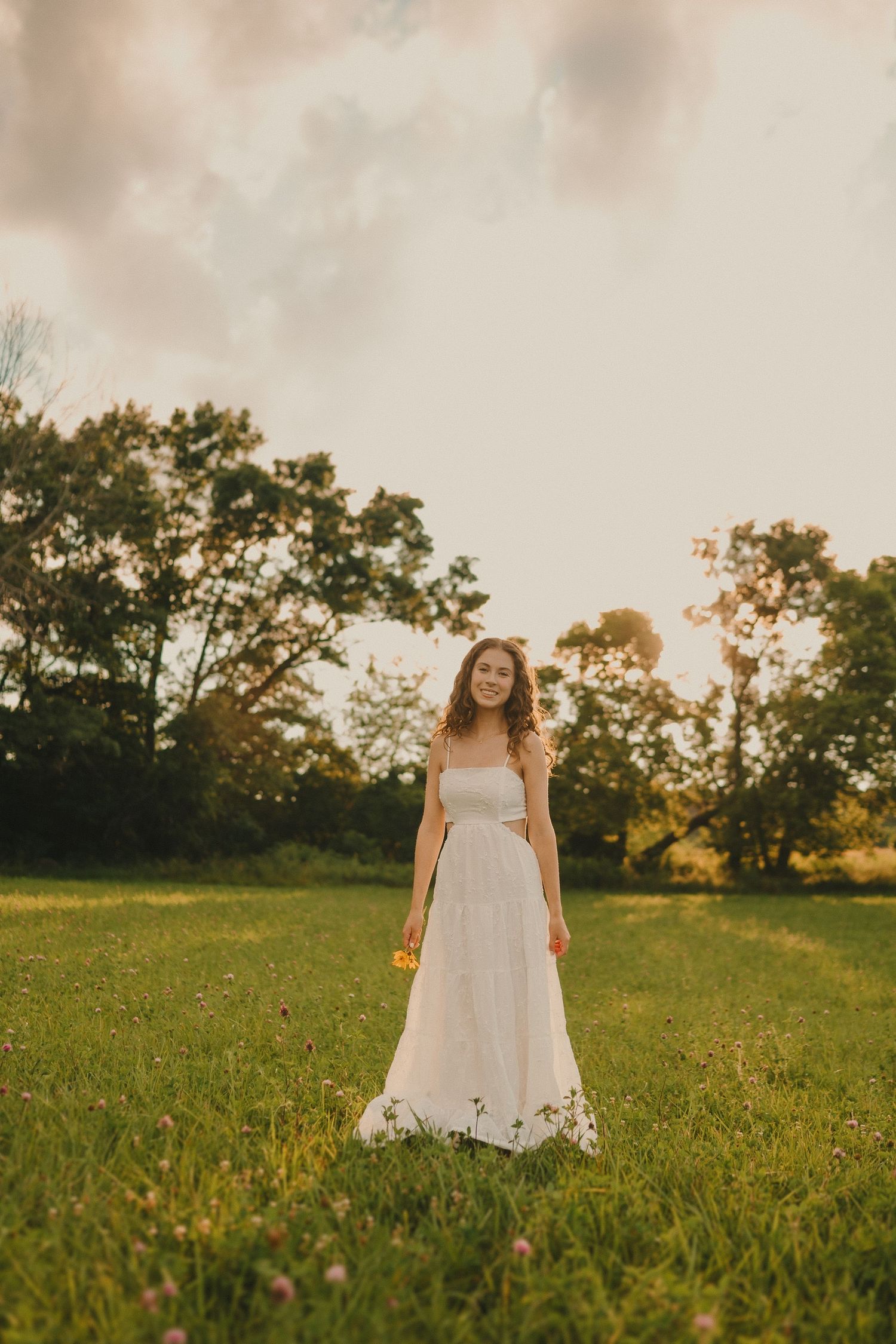 An ethereal portrait in a white dress standing among wildflowers during sunset.