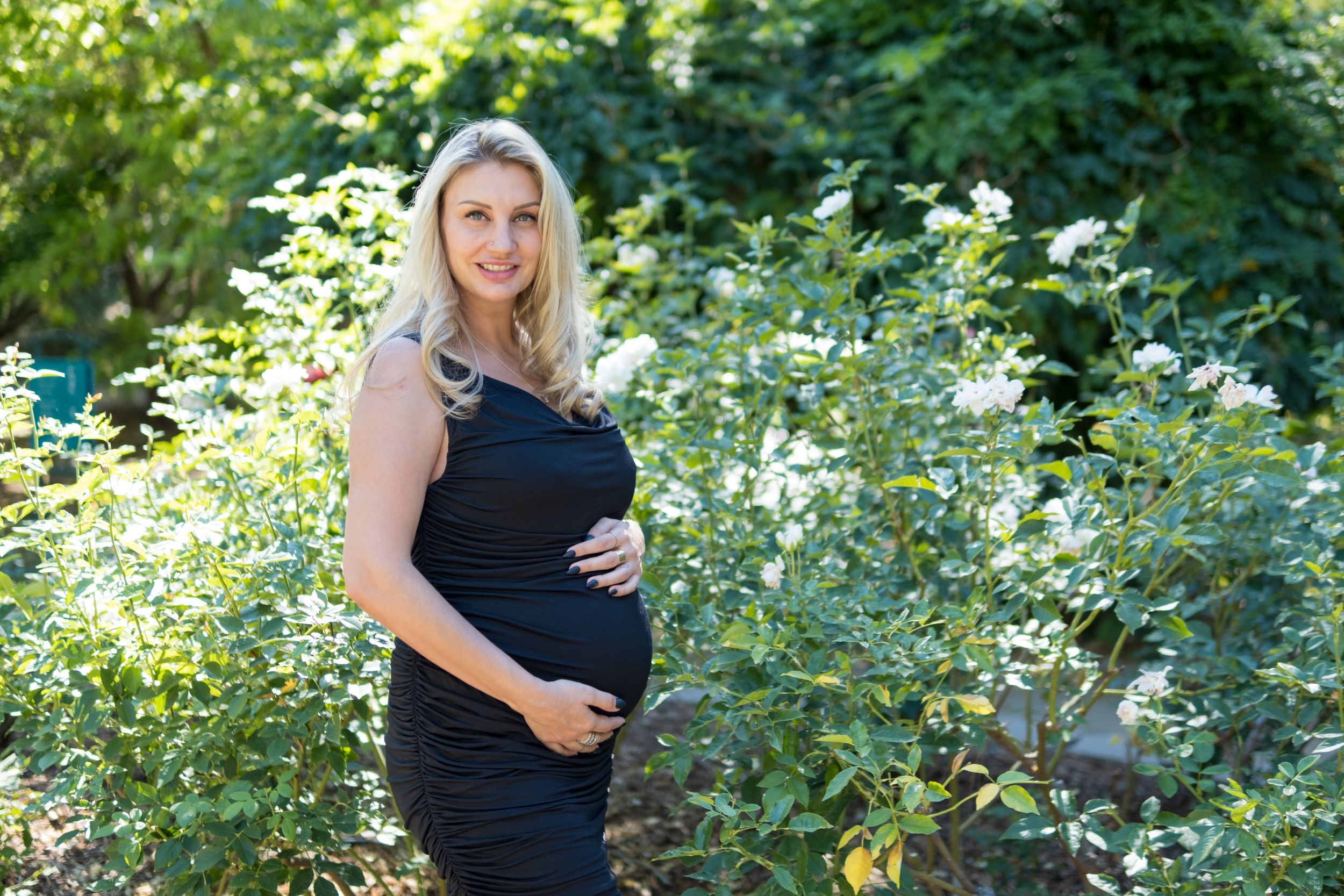 Beautiful maternity photo taken outdoors with sunlit white flowers and green foliage in the background.