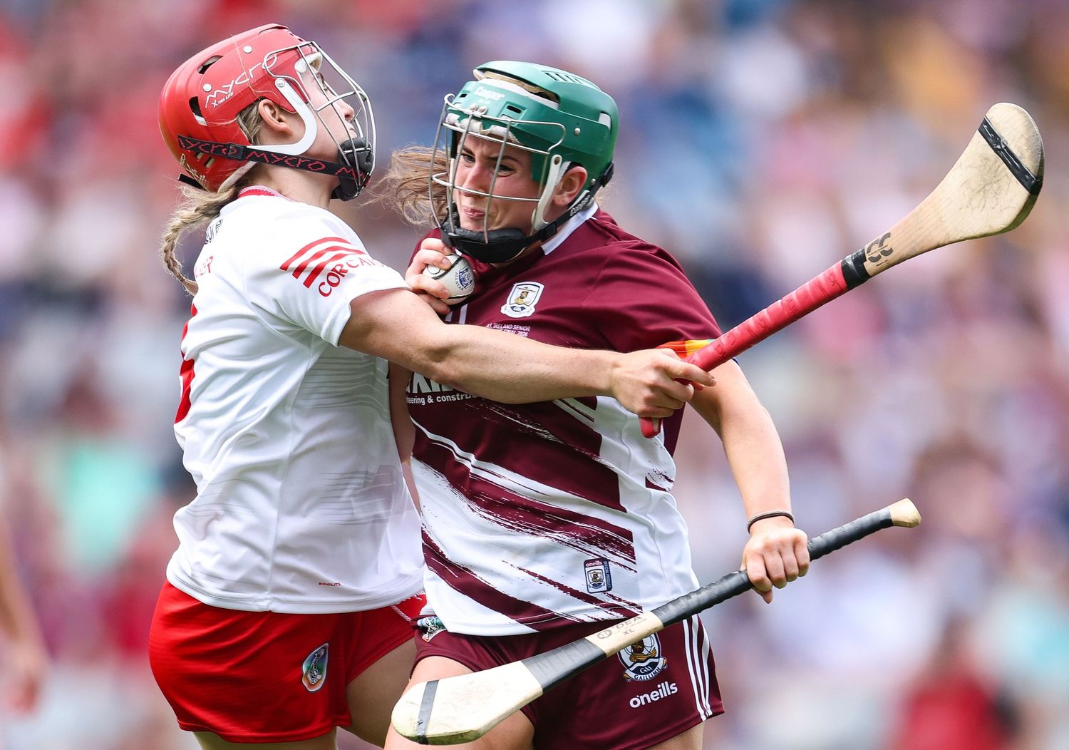 Two hurling players compete for the ball during an intense match, one in white and red, the other in maroon and white.