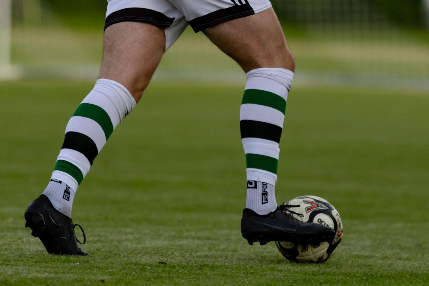 Close-up of soccer player's legs with striped socks and ball on grass field.