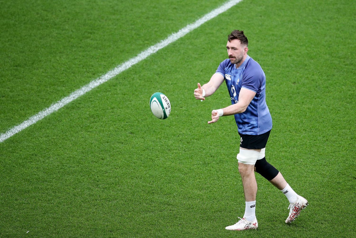 Rugby player in blue jersey prepares to pass the ball on a green field during training session.