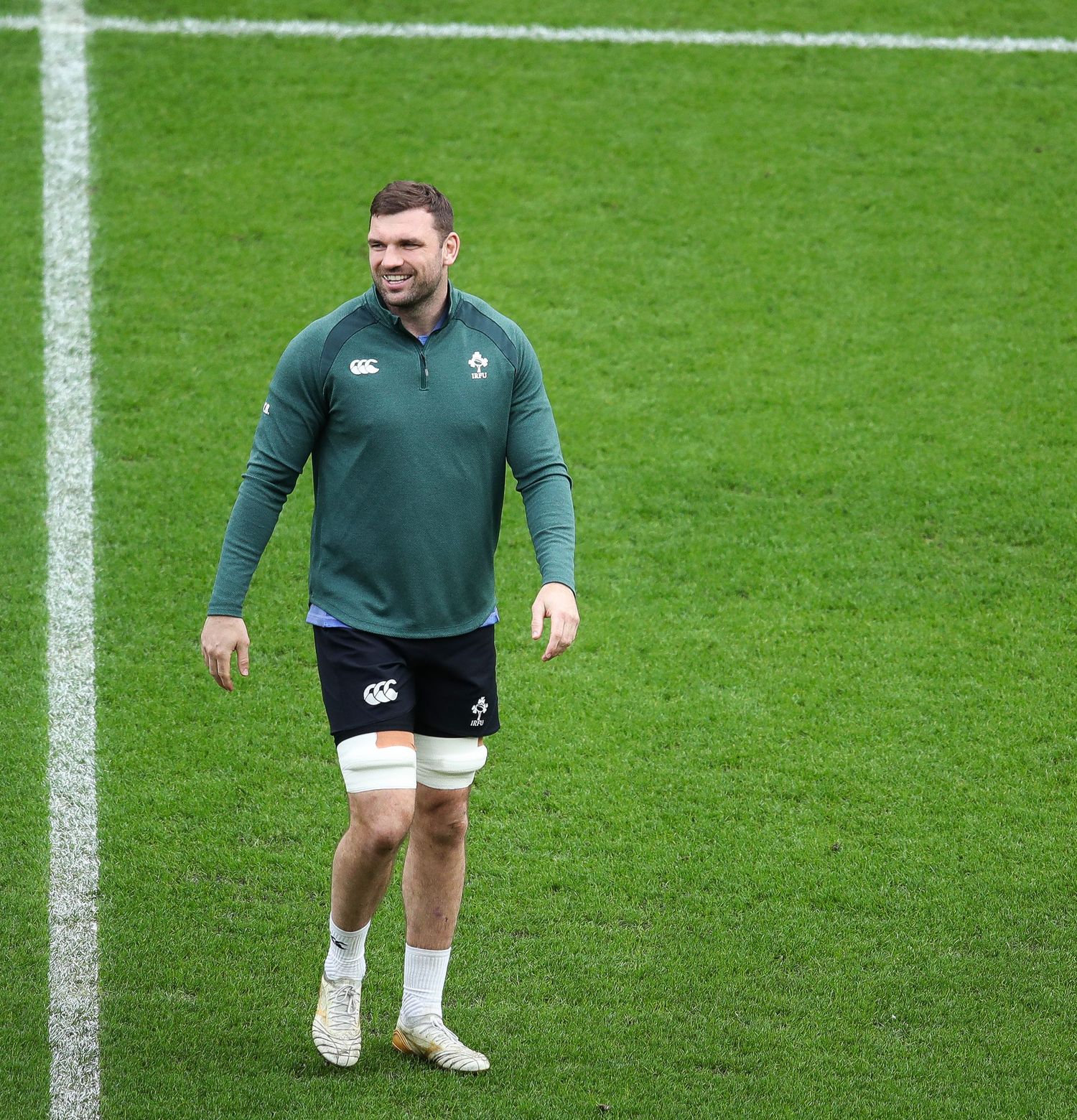 Rugby player in green uniform performs stretching exercises on grass field during training session.