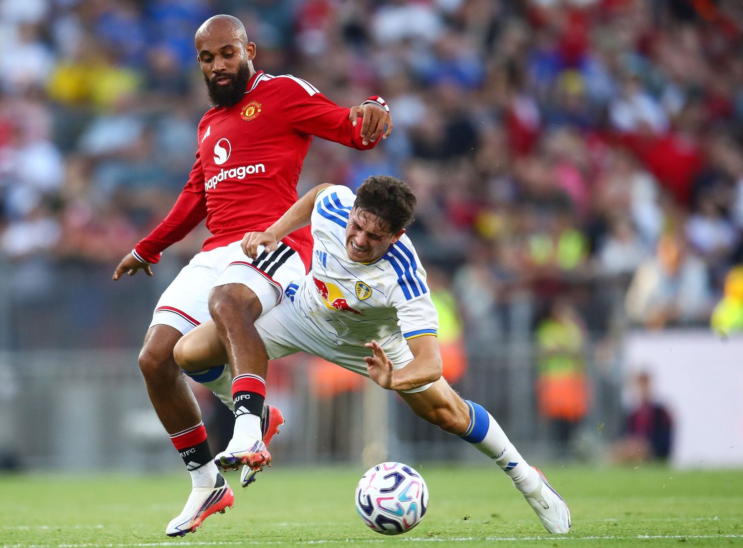 Two soccer players compete for the ball, one in red Manchester United kit, another in white, during a match.