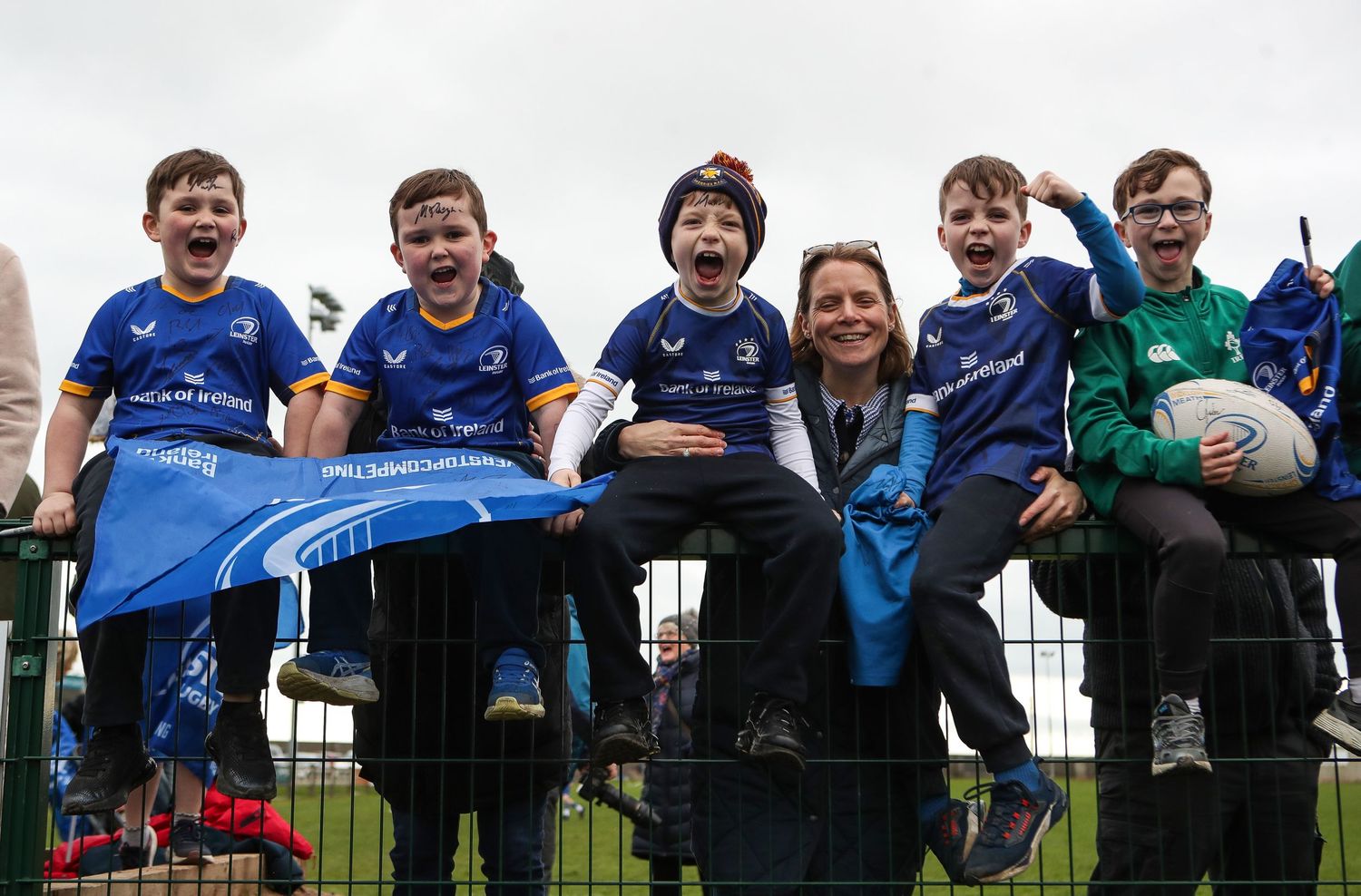 A group of young athletes in blue sports uniforms sit together on bleachers at a sporting event.