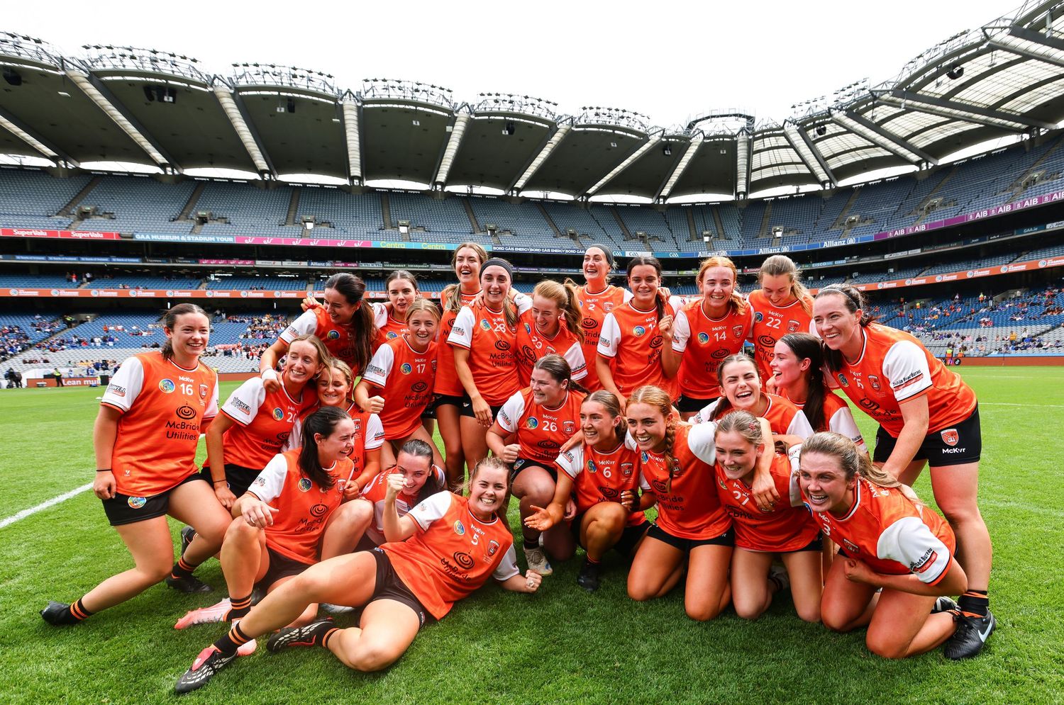 Women's Gaelic football team celebrating victory at Croke Park stadium, posing together in orange jerseys.