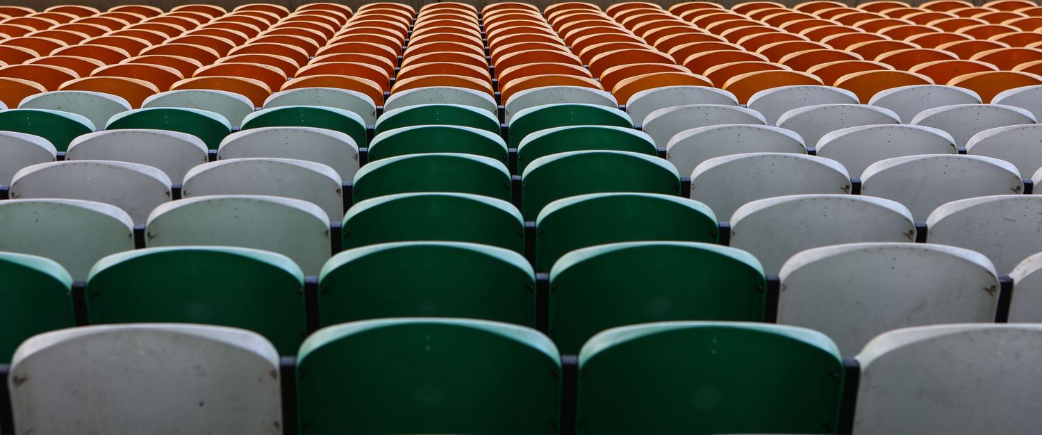 Rows of colorful stadium seats in green, white, and orange arranged in a pattern at an empty sports arena.