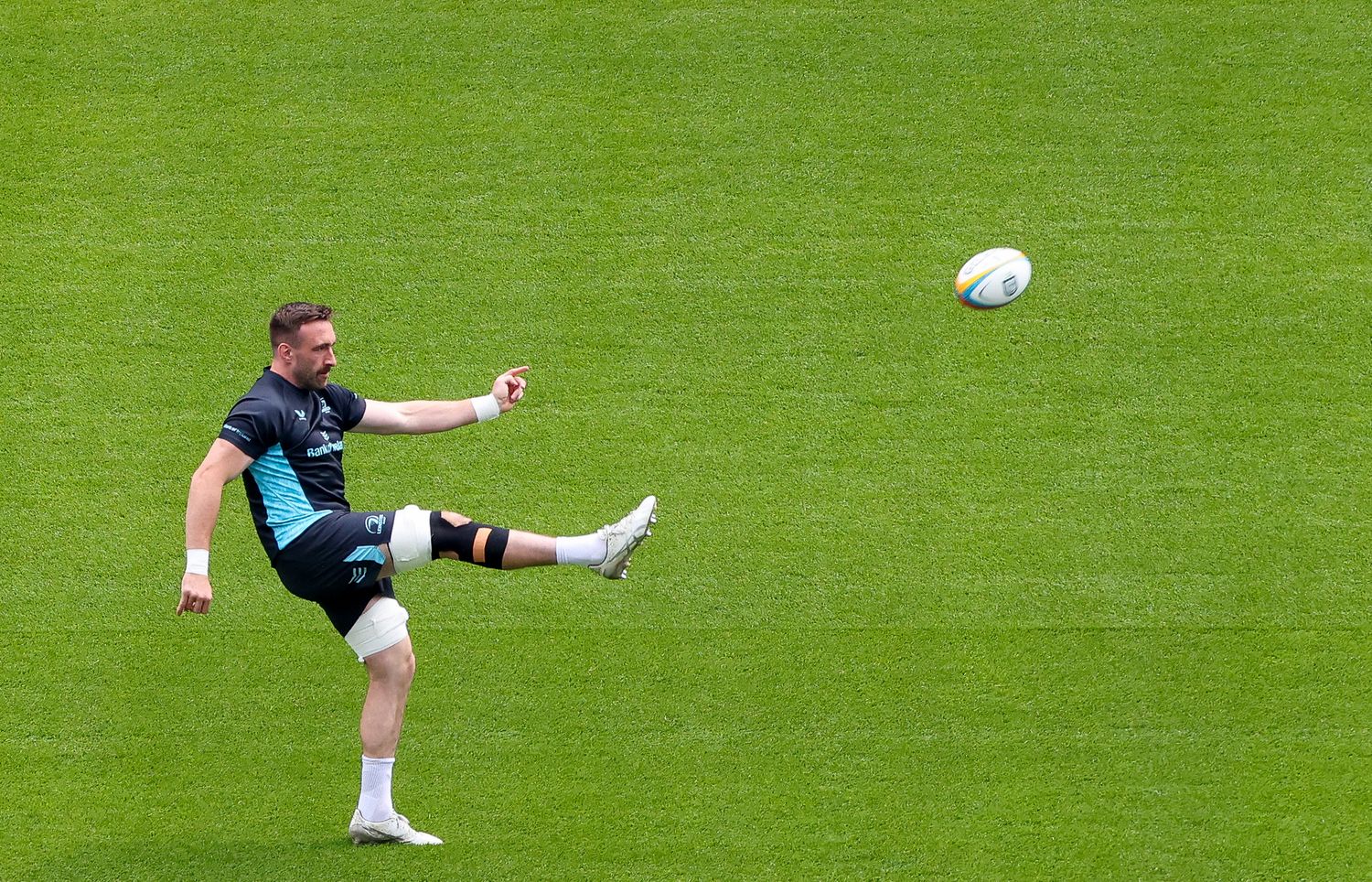Rugby player kicking a ball on a green grass field during training session.