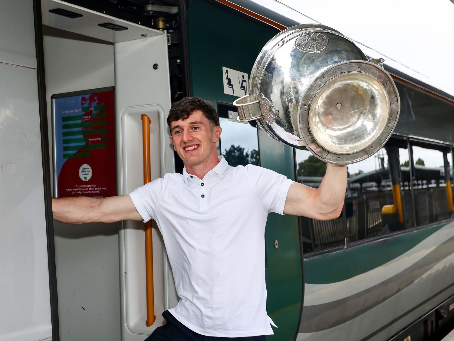 Young man proudly holding a large silver trophy cup while standing at the door of a green train.