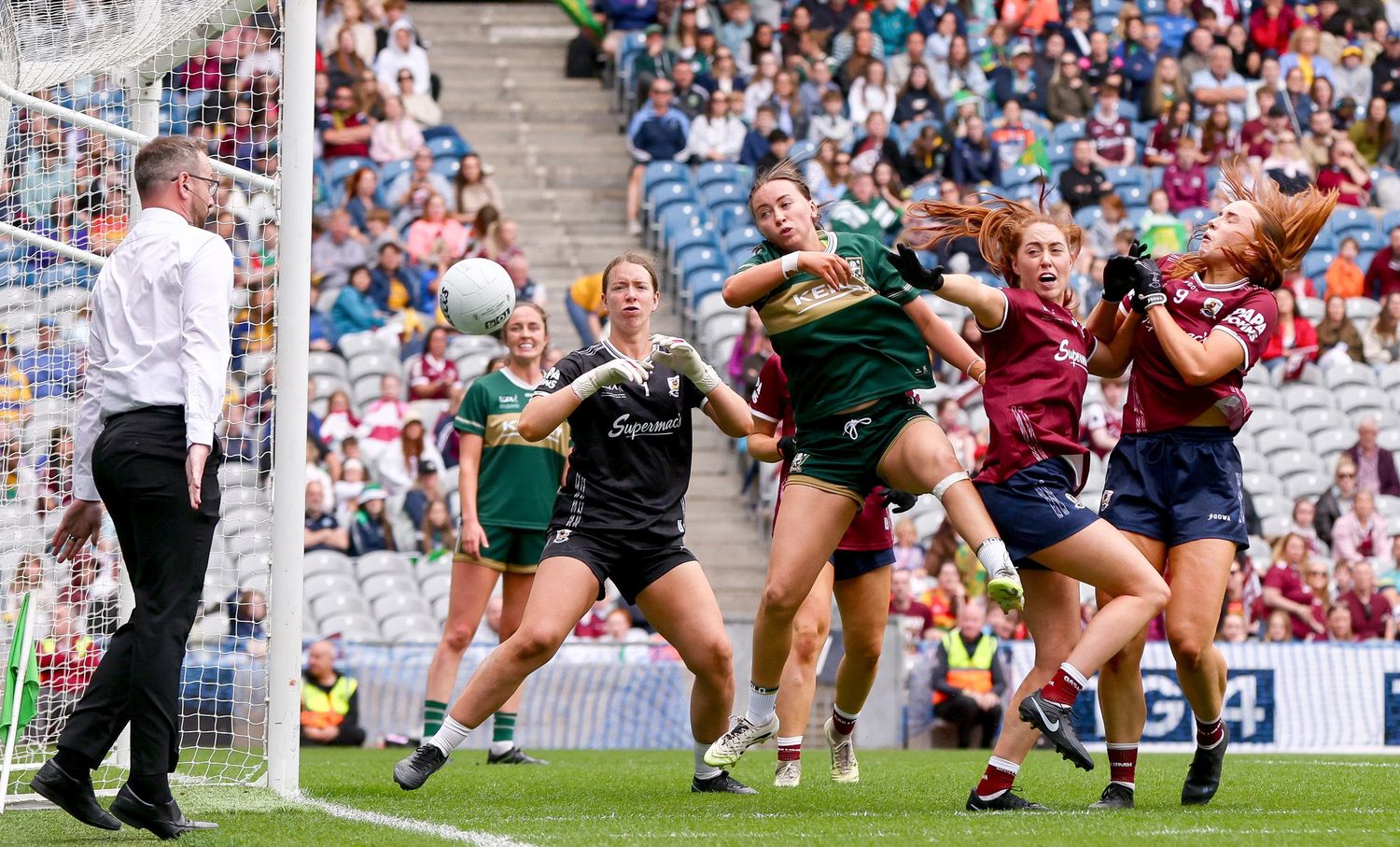 Women's Gaelic football players compete for the ball during an intense match at a packed stadium.