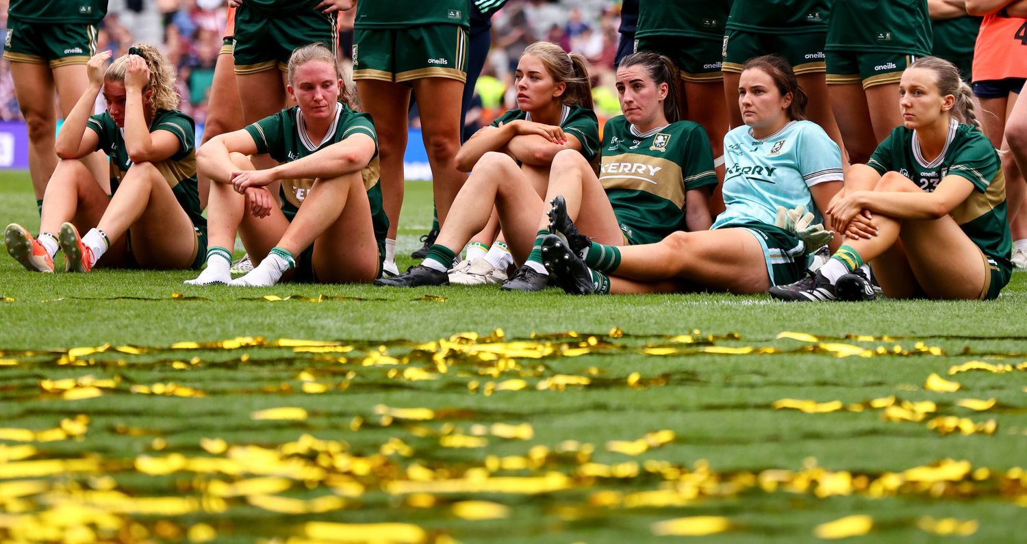 Dejected female rugby players sit on the field surrounded by gold confetti after losing a championship final.