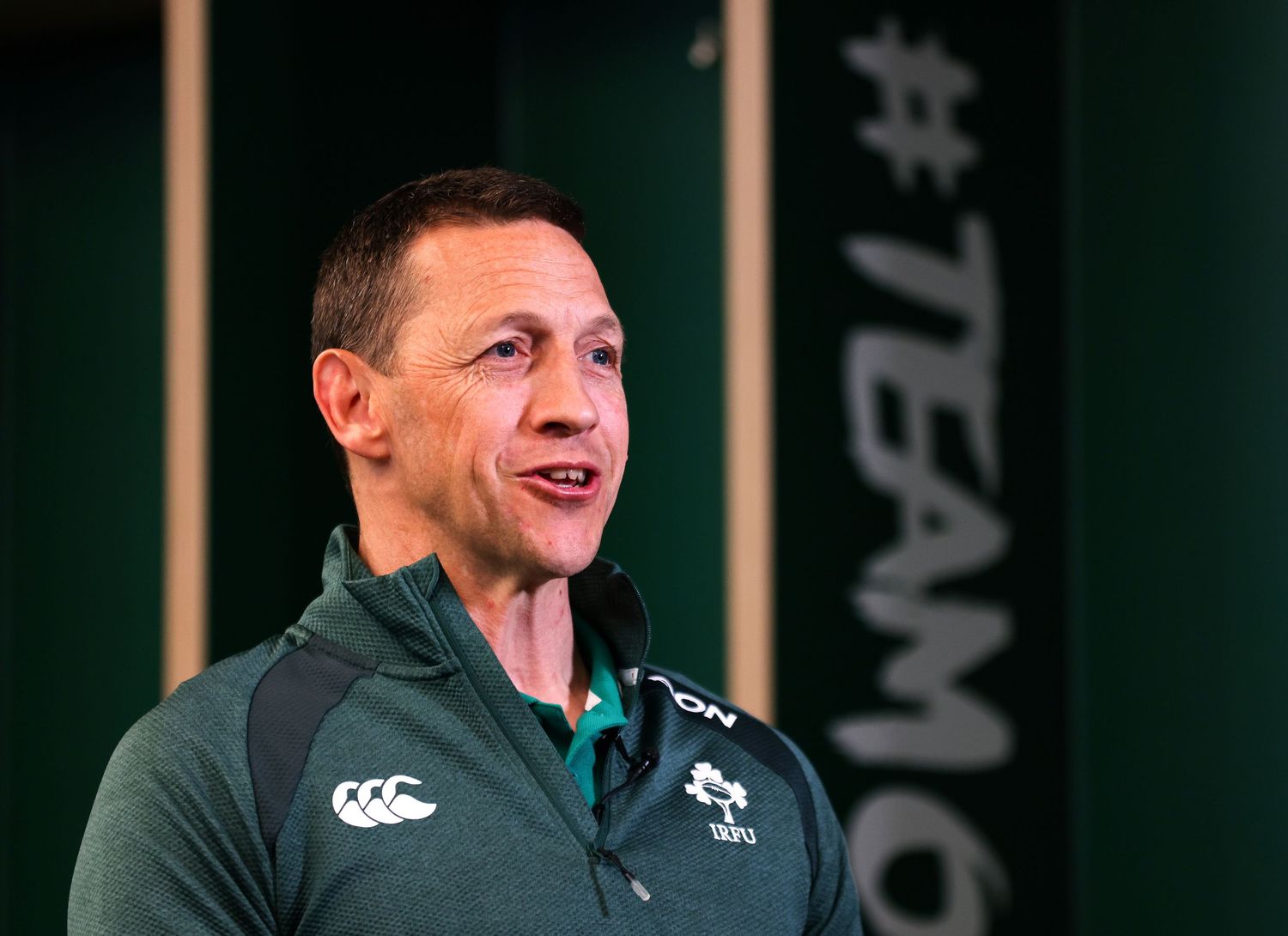 Man in green Canterbury rugby jersey speaks at Ireland team event with #TEAMI backdrop.
