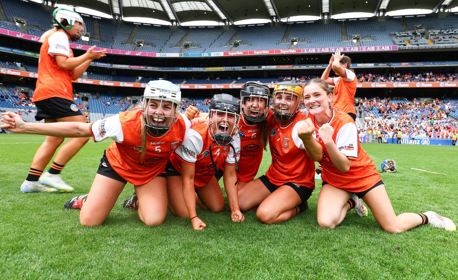 Female camogie players in orange uniforms celebrate victory together on the field at Croke Park stadium.