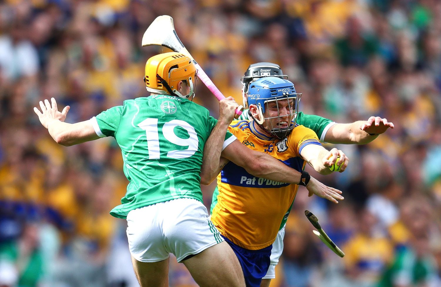 Two hurling players compete for the ball during an intense GAA match, wearing green and yellow jerseys.