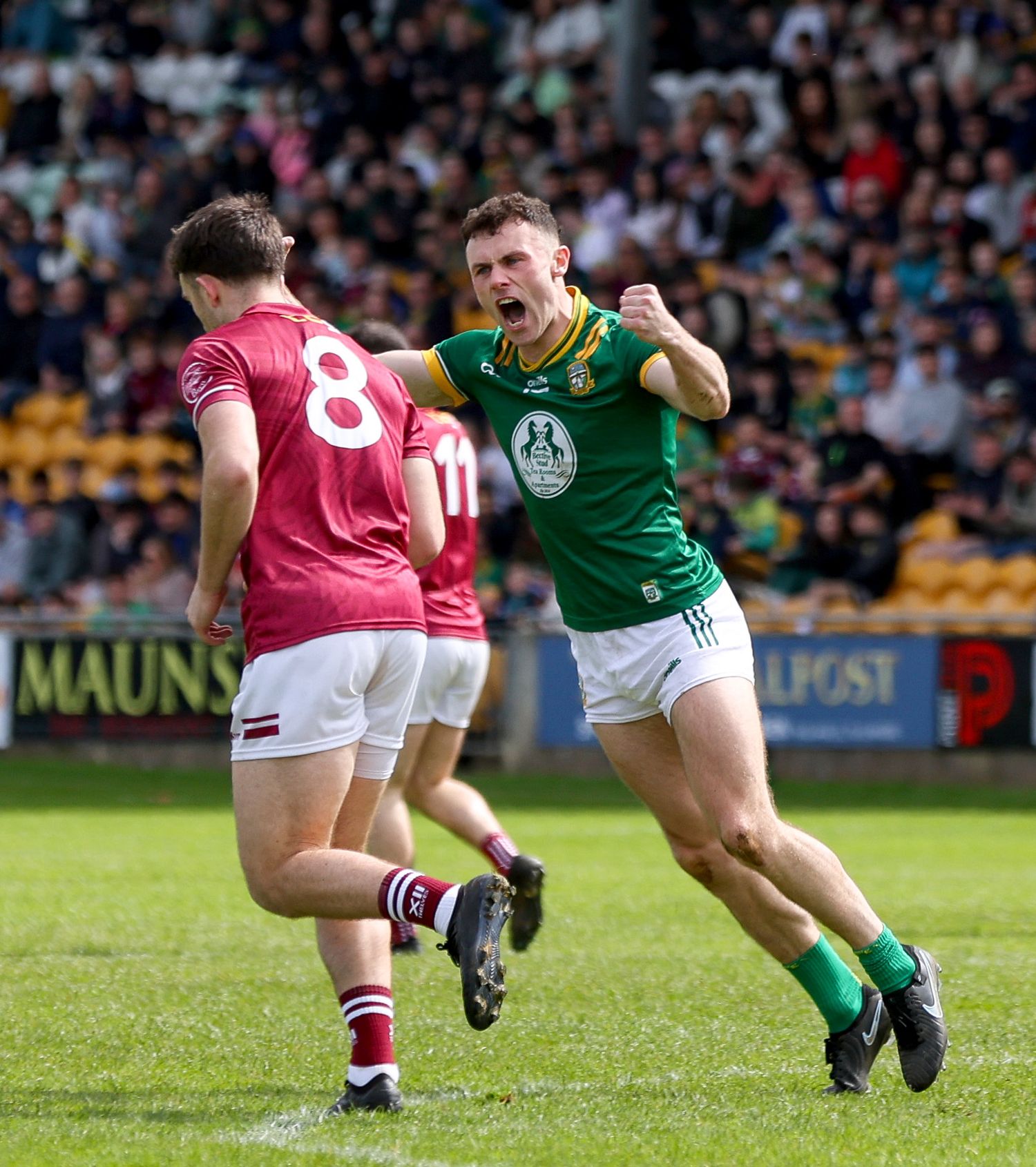 GAA footballer in green jersey celebrates with fist pump during Gaelic football match on grass pitch.