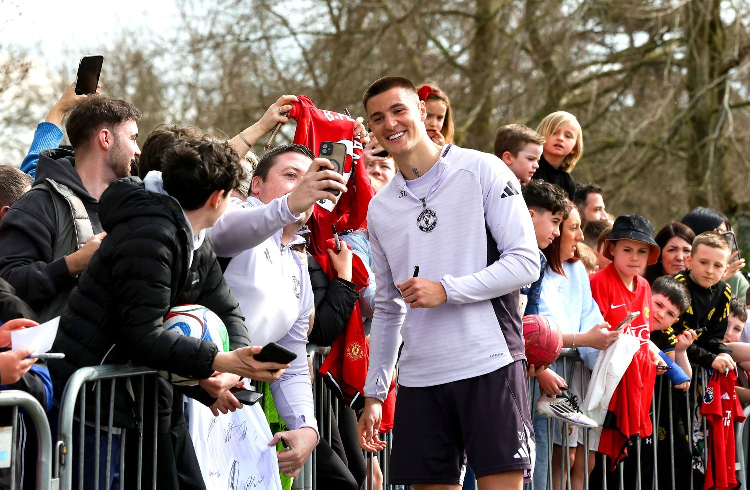 Manchester United player takes selfie with fans behind barriers at outdoor event, wearing purple training kit.