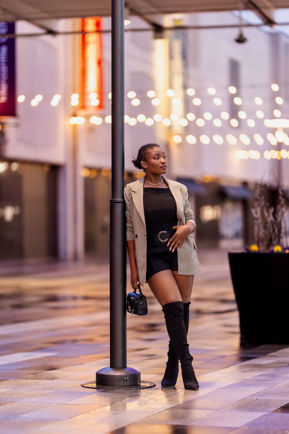 Fashion portrait in an urban setting with string lights and modern architecture.