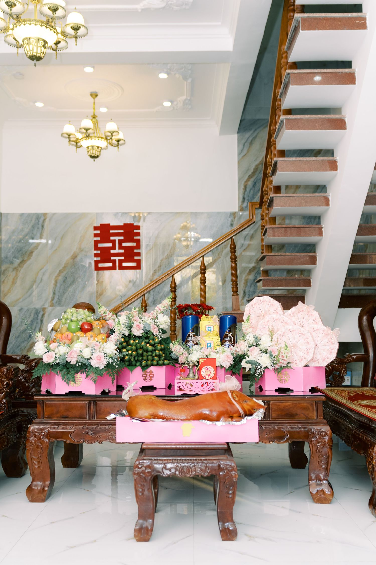 Traditional wedding decorations featuring pink floral arrangements in wooden boxes on ornate tables under crystal chandeliers.
