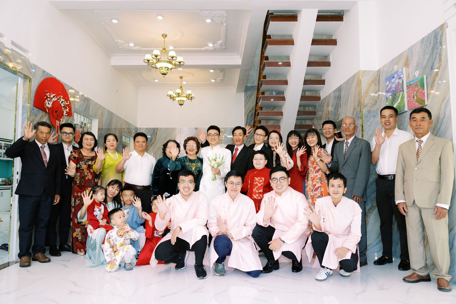A large group photo taken indoors with a decorative staircase and bright interior lighting in the background.