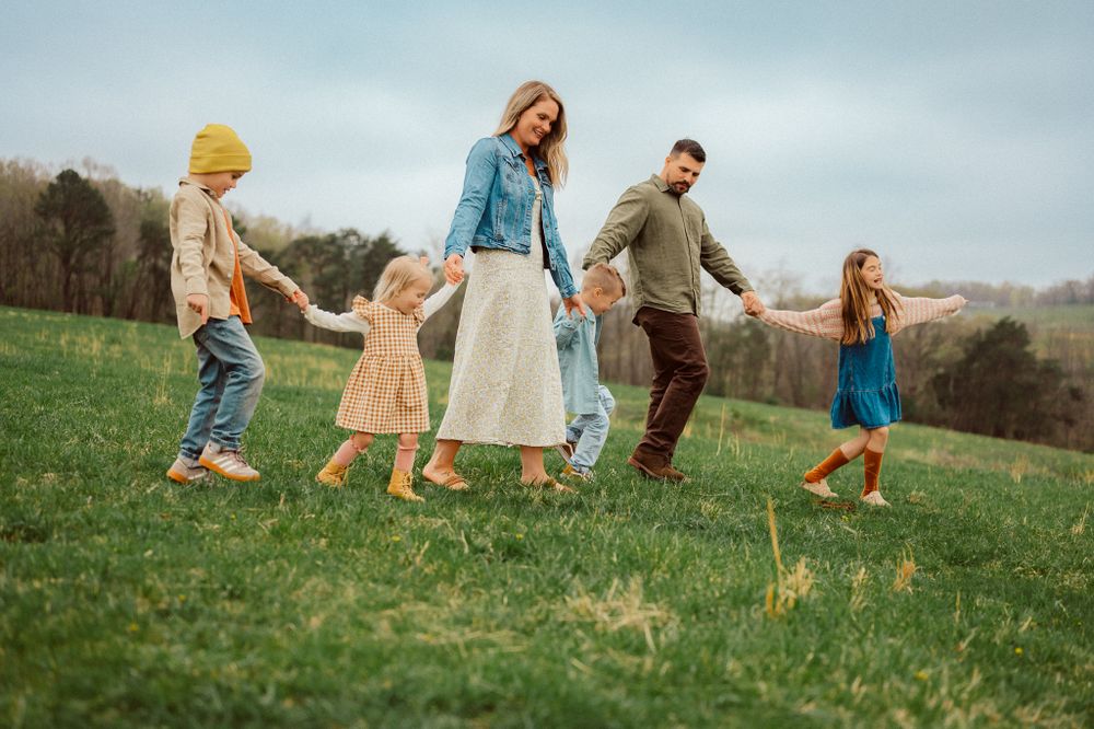 Family holding hands while skipping through grassy hillside on autumn afternoon.