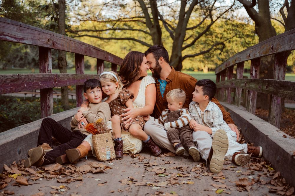 Family gathered on wooden bridge surrounded by fall foliage during outdoor photoshoot.