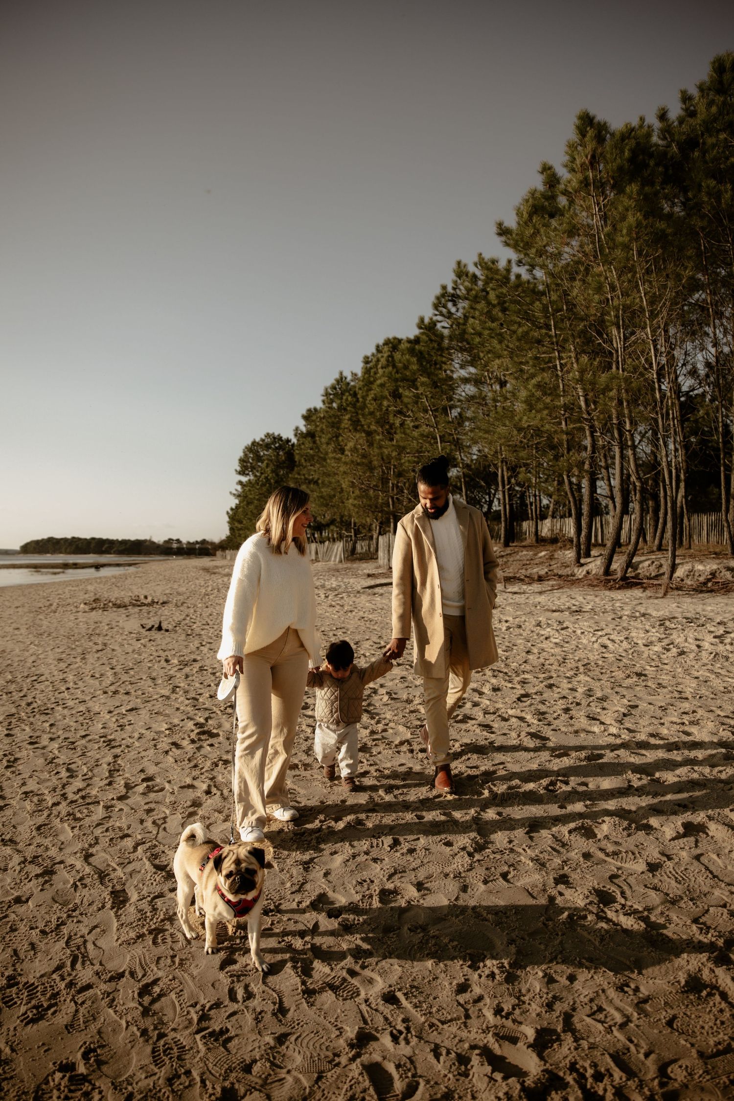 Family walking on beach with small dog in matching cream outfits.