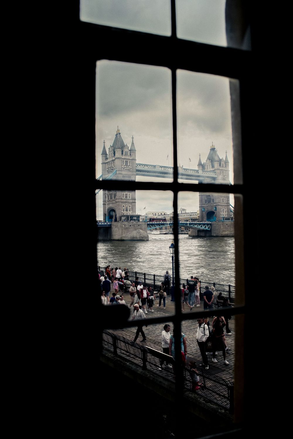 View of London's Tower Bridge through a divided window frame on a cloudy day.
