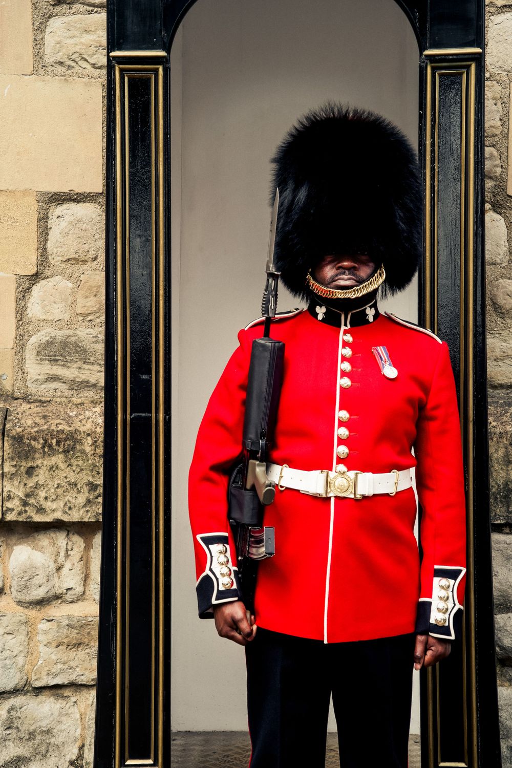 Royal guard in traditional red uniform and bearskin hat standing at attention in ceremonial post.