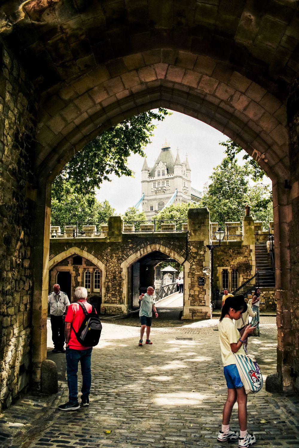 Historic stone archway leading to Tower Bridge with tourists walking through the passage.
