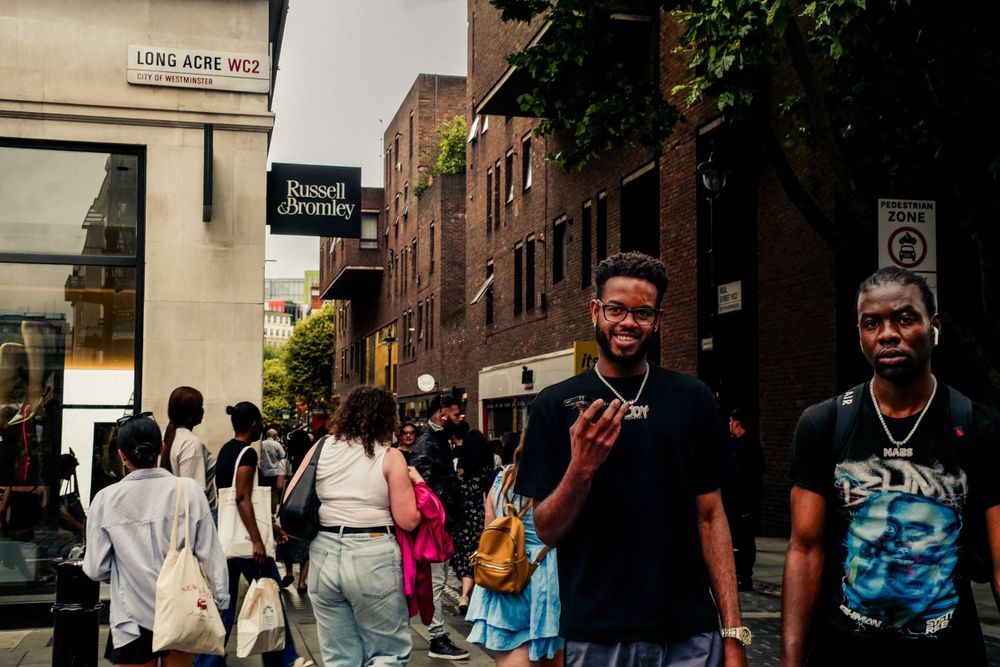 People walking on a busy urban street with brick buildings and storefronts in the background.