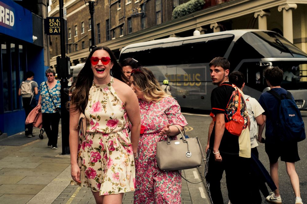 Summer crowd walking down a city street wearing floral dresses on a sunny day.