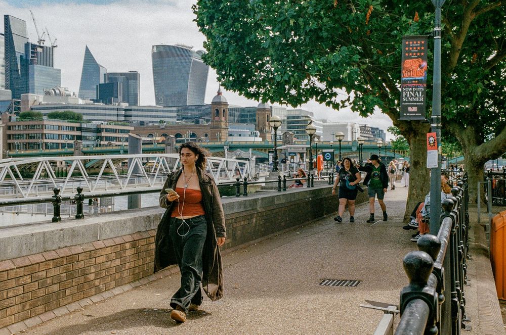 Person walking along the Thames riverside path with London's modern skyline in the background.