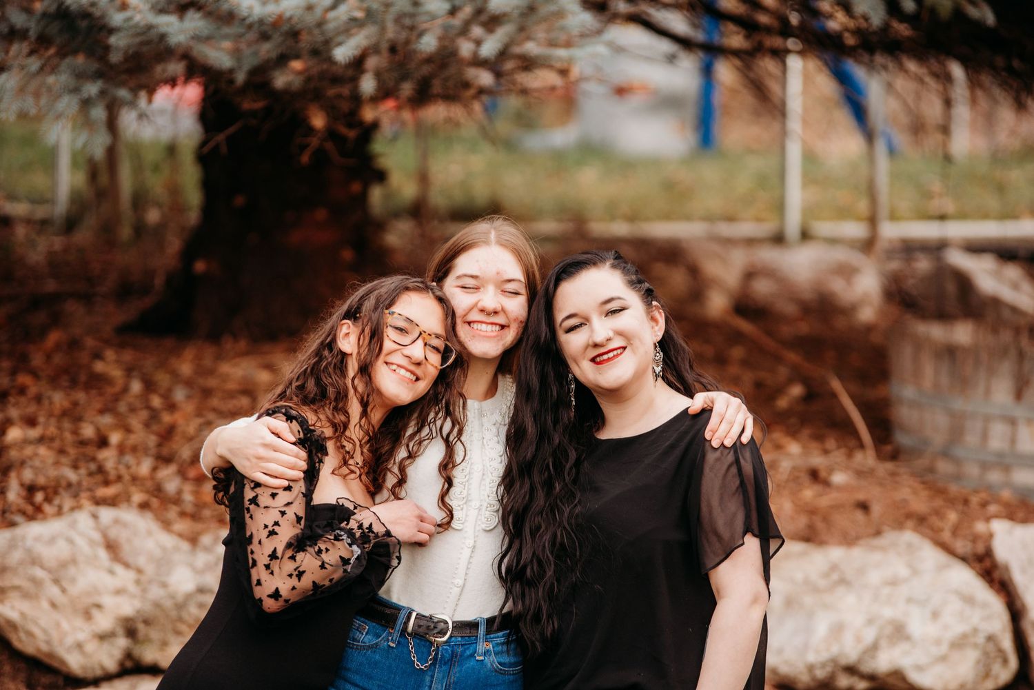 Three friends hugging and smiling together outdoors during autumn.