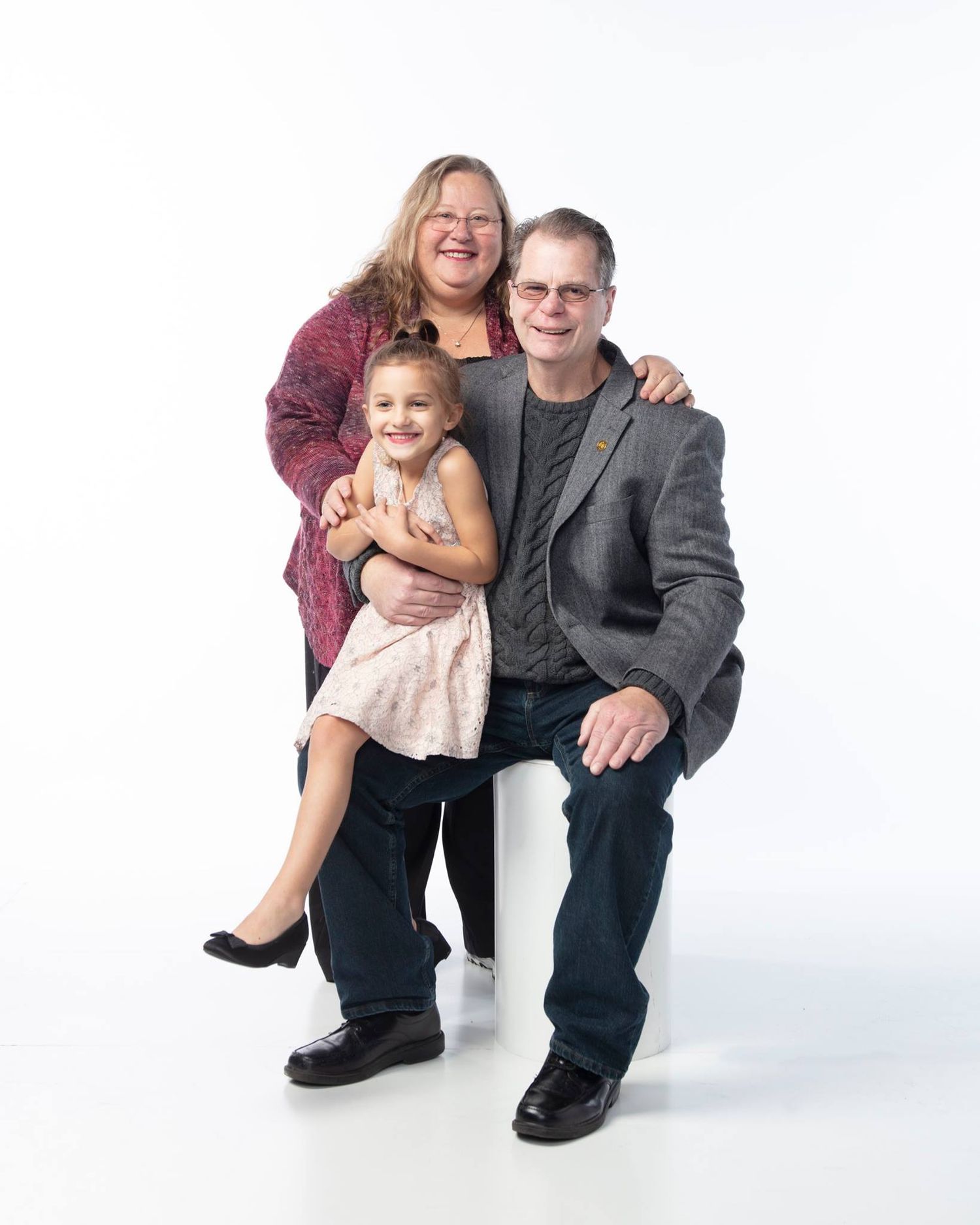Family portrait of three people wearing casual attire against white background posing together and smiling.