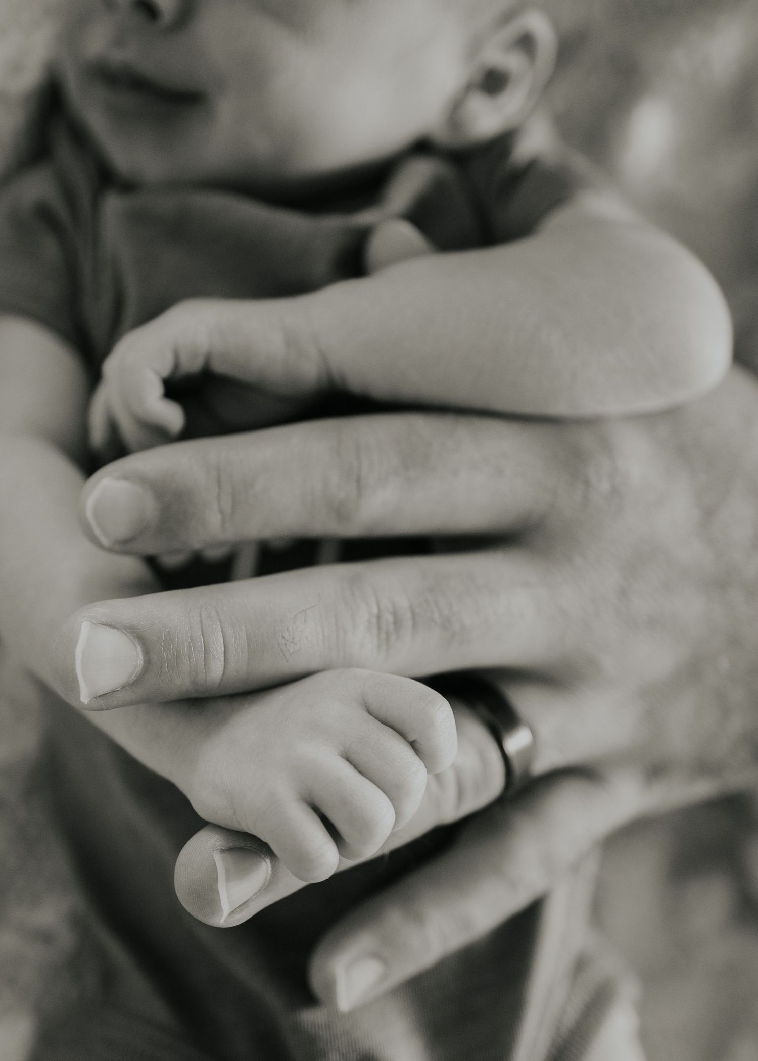 A close-up black and white photograph shows a tiny baby's hand gently holding an adult's finger.