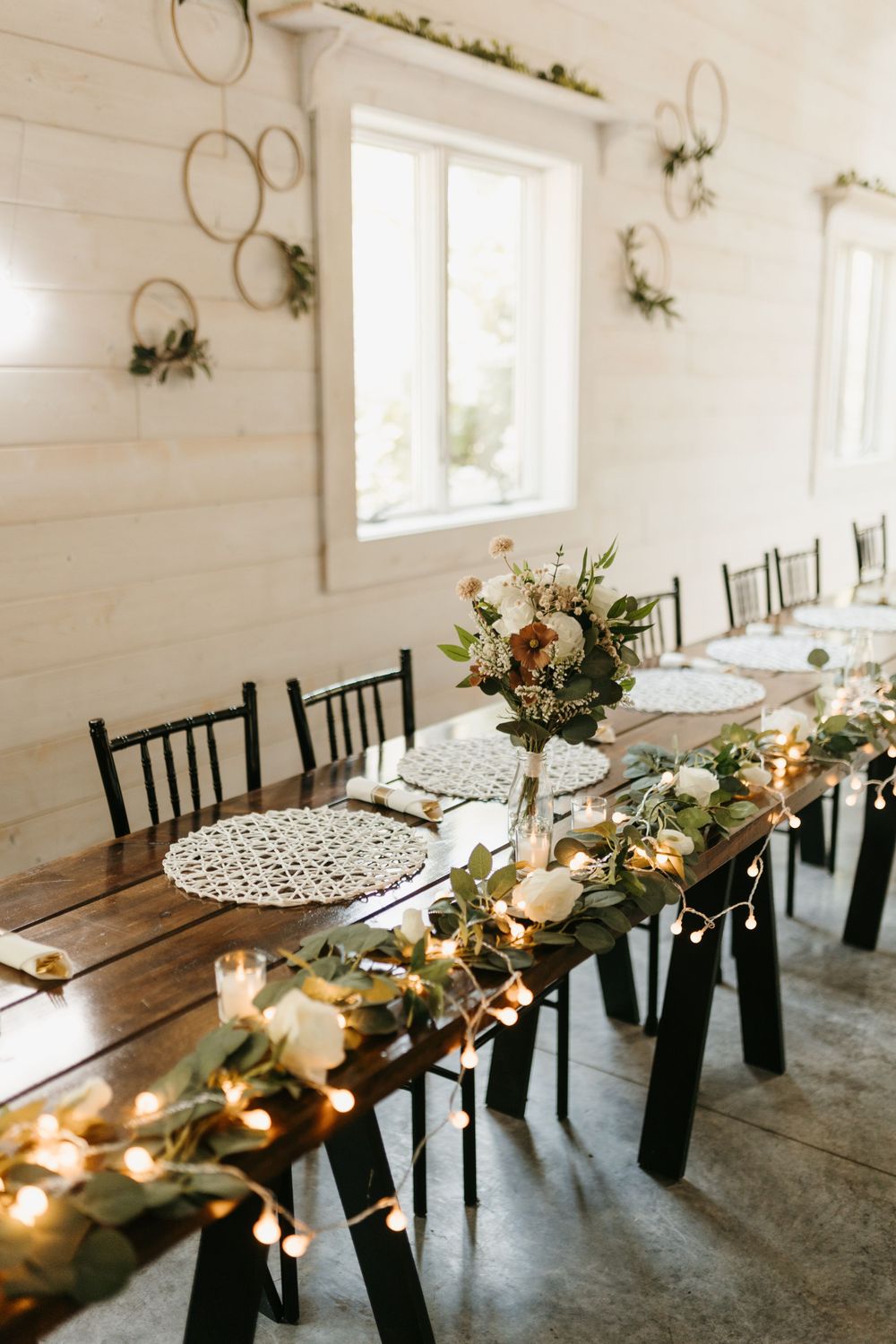 Elegant wedding head table with greenery garland, fairy lights, floral centerpiece, and hoop decor.