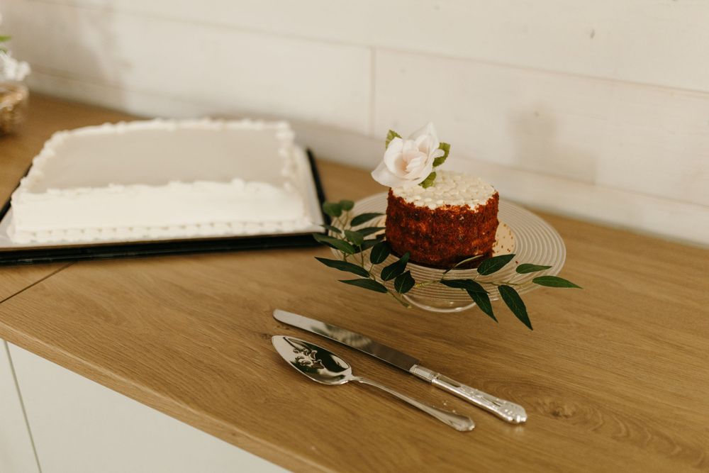 Wedding dessert table with red velvet cake topped with a rose on a glass stand beside a sheet cake.