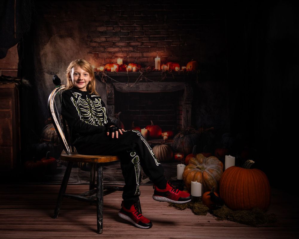 Halloween photo of a costume against dark brick wall with glowing fireplace and pumpkin decorations.