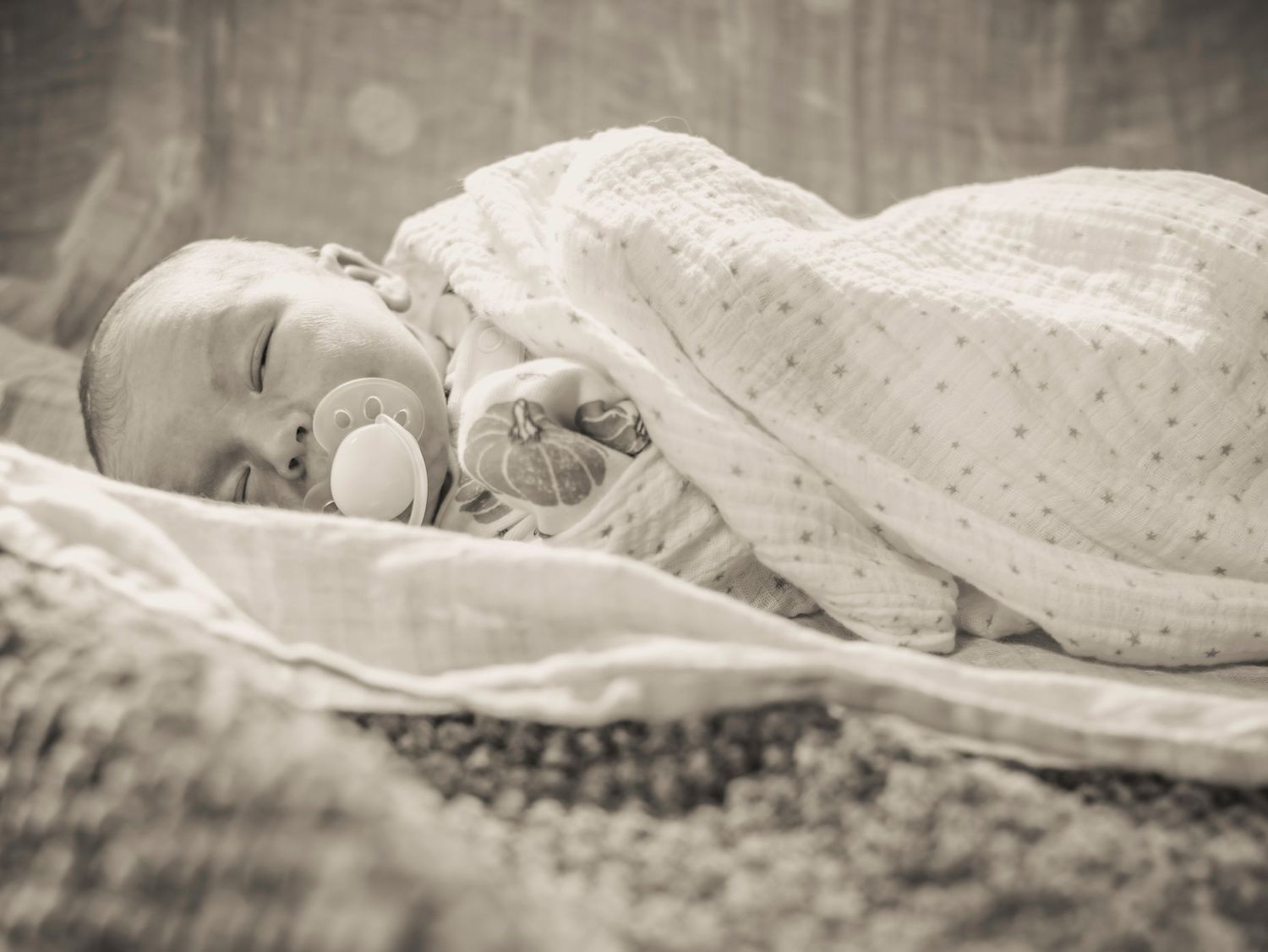 Peaceful sleeping newborn wrapped in polka dot blanket in black and white.
