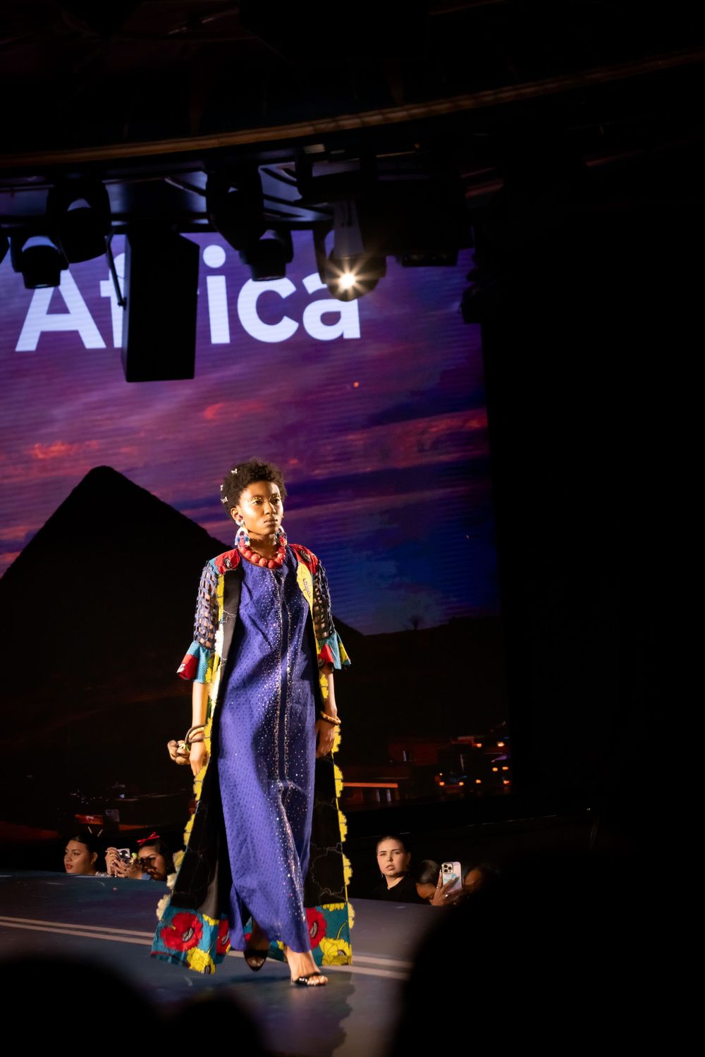 Fashion model in blue gown walking runway with Africa text display in background.