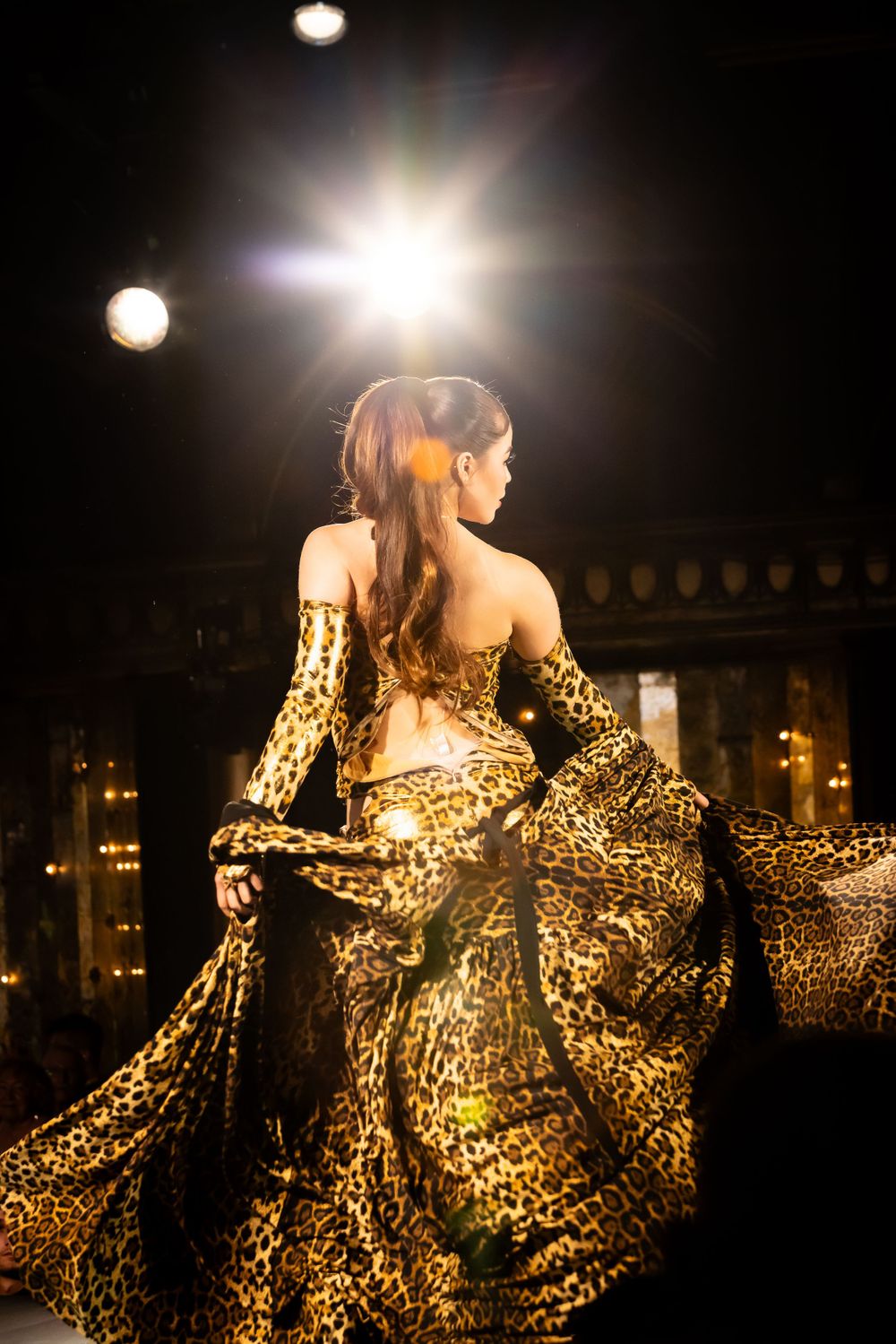 Fashion model wearing a glamorous gold leopard print evening gown under dramatic stage lighting.