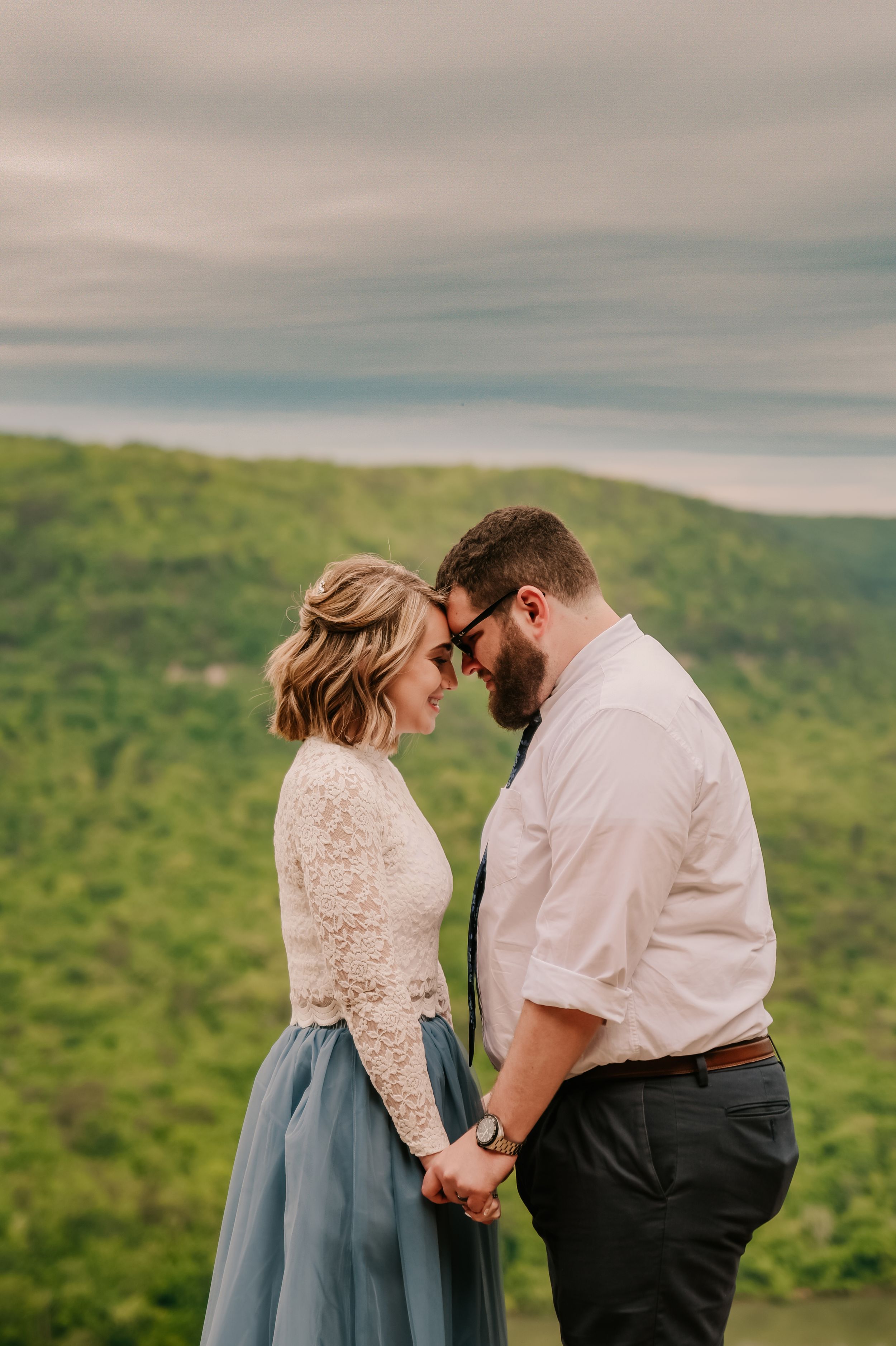 A tender moment shared between a couple in formal wear on a scenic mountain overlook.