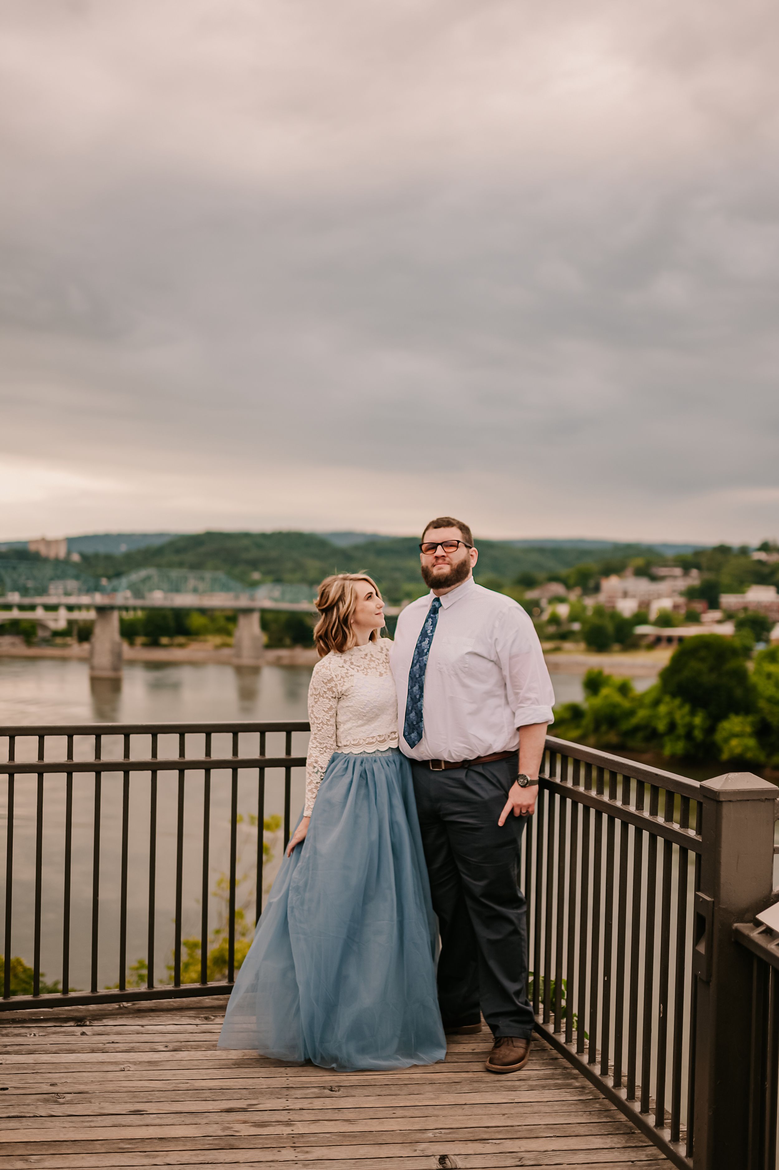 A couple shares a romantic moment on a riverside observation deck with mountain views.