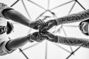 Black and white close-up of hands joined together in unity against geometric architectural background.