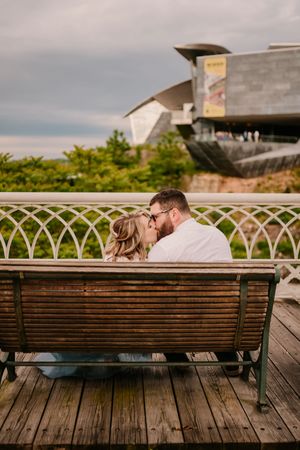 A couple shares an intimate moment on a wooden bench overlooking an architectural landmark.