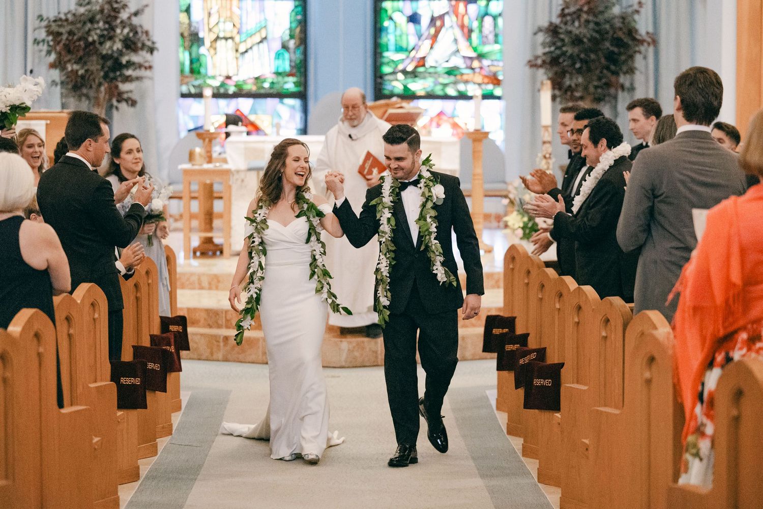 A joyful couple walks down the church aisle after their wedding ceremony while guests look on from wooden pews.
