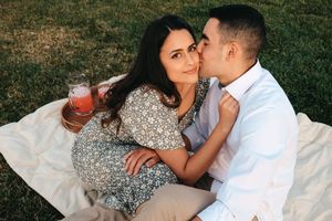A couple enjoying a picnic on a blanket with drinks outdoors.
