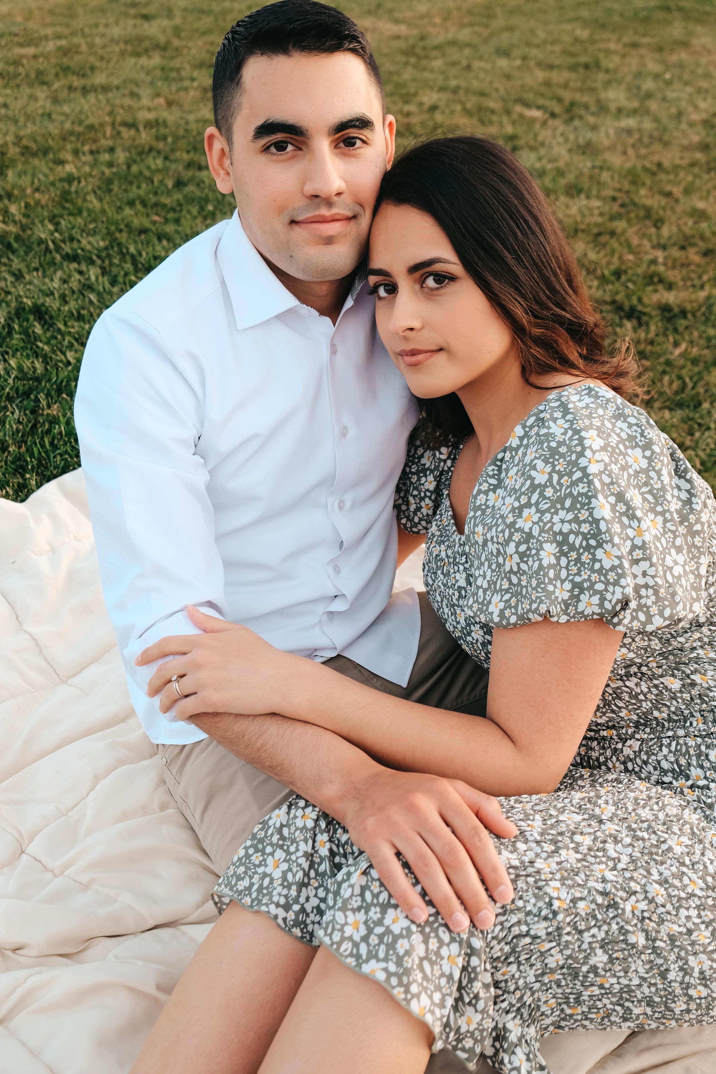 A couple poses together on a white blanket during an outdoor photoshoot.