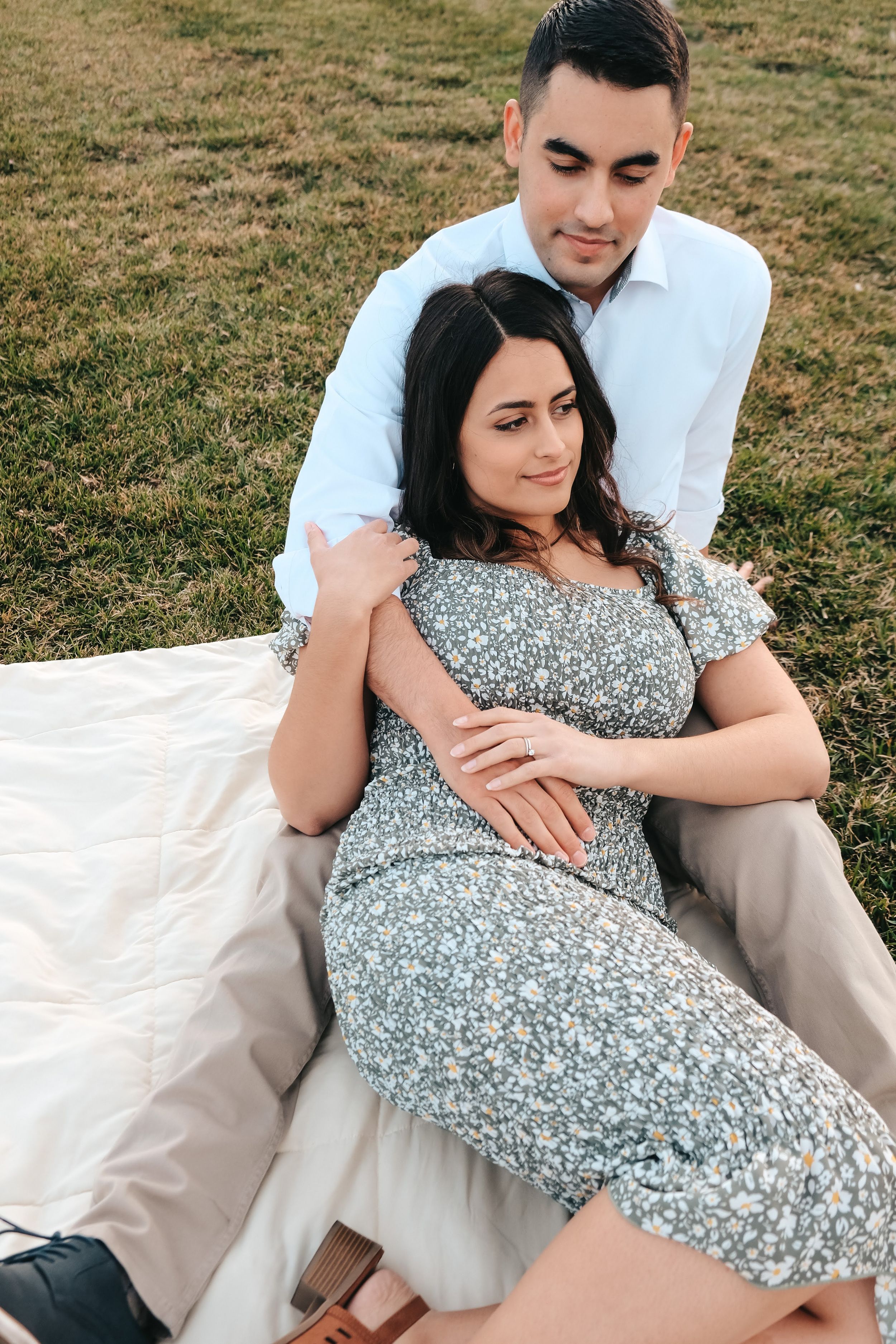 A couple relaxing together on a white blanket in a sunny field.