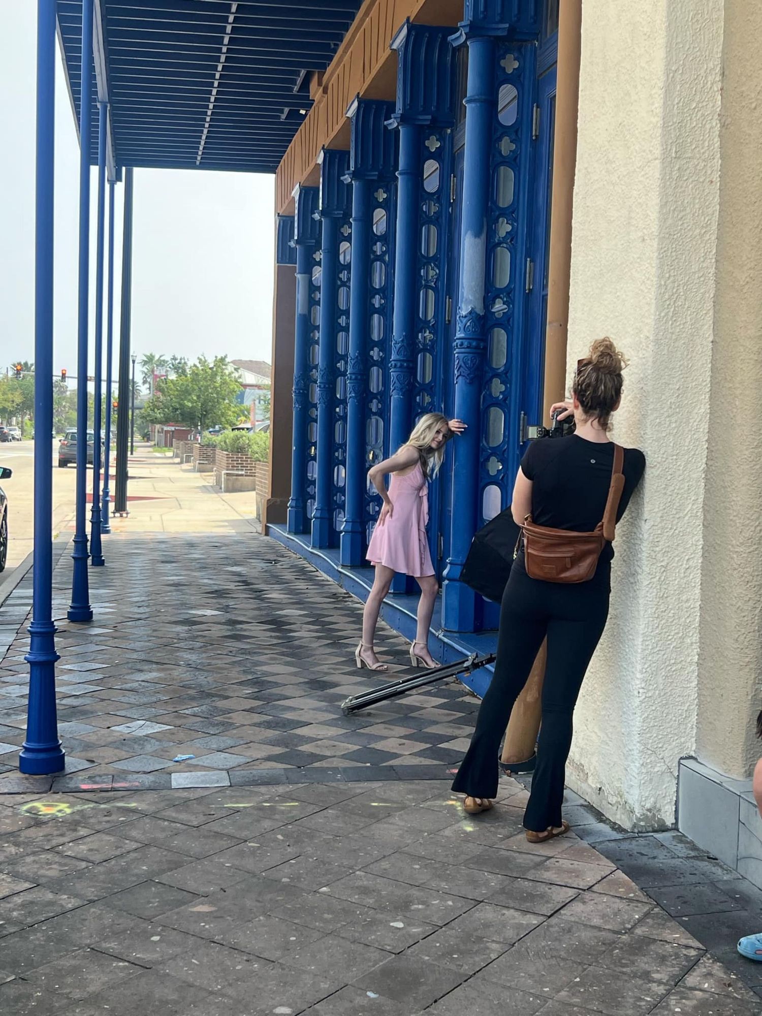 People examining distinctive blue architectural columns along a covered outdoor walkway with stone flooring.